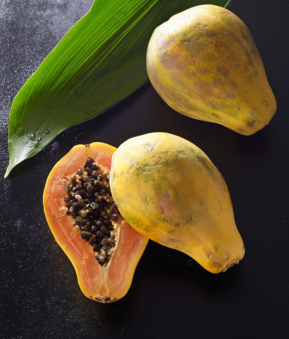 Two papayas, one halved, with a palm leaf