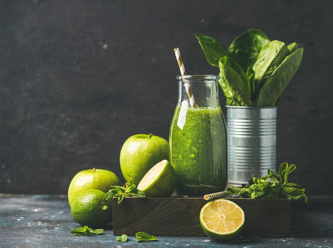 Green smoothie in bottle with apple, romaine lettuce, lime and mint on dark background