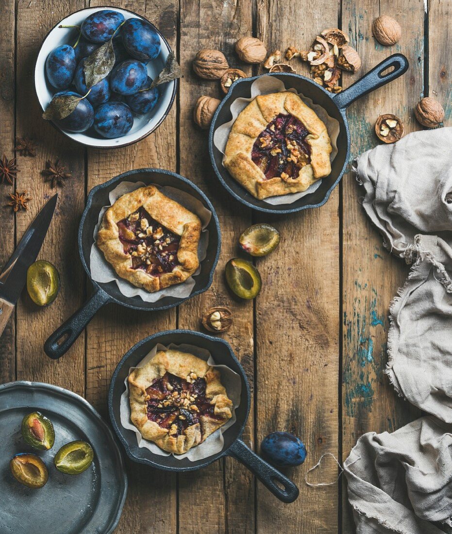 Plum and walnut crostata pie in individual cast iron pans over rustic wooden table