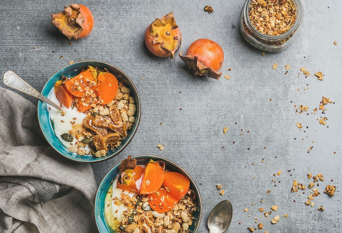 Healthy vegetarian breakfast: Oatmeal, quinoa granola with yogurt, dried fruit, seeds, honey, fresh persimmon in bowls