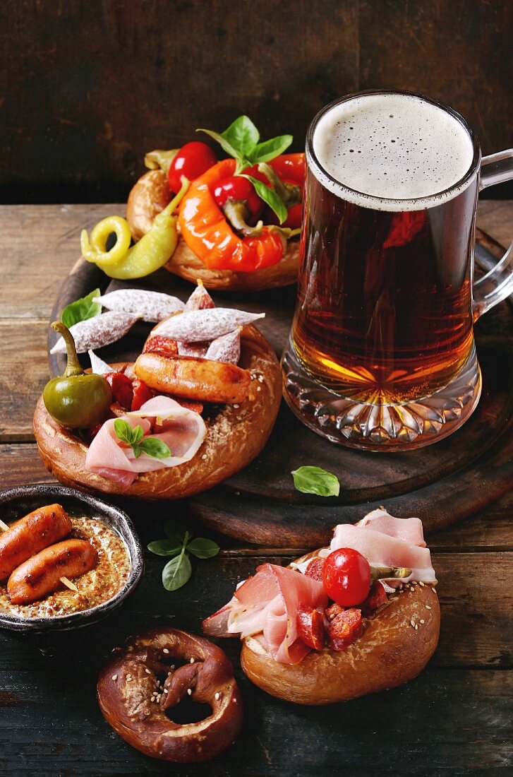 Fried sausages, wienerwurst, ham, marinated chili peppers in salted pretzels with basil and glass of lager beer