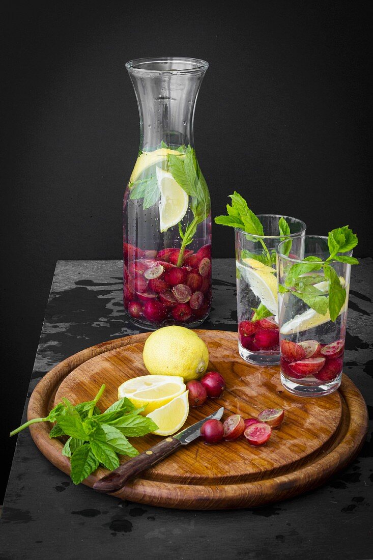 Wasserkrug mit Stachelbeeren, Kräutern und Zitrone auf Schiefertisch