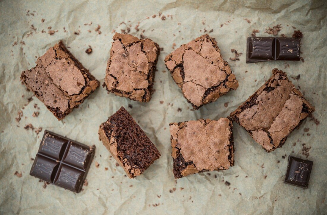 Schokoladen-Brownies und Schokoladenstücke auf Backpapier (Aufsicht)