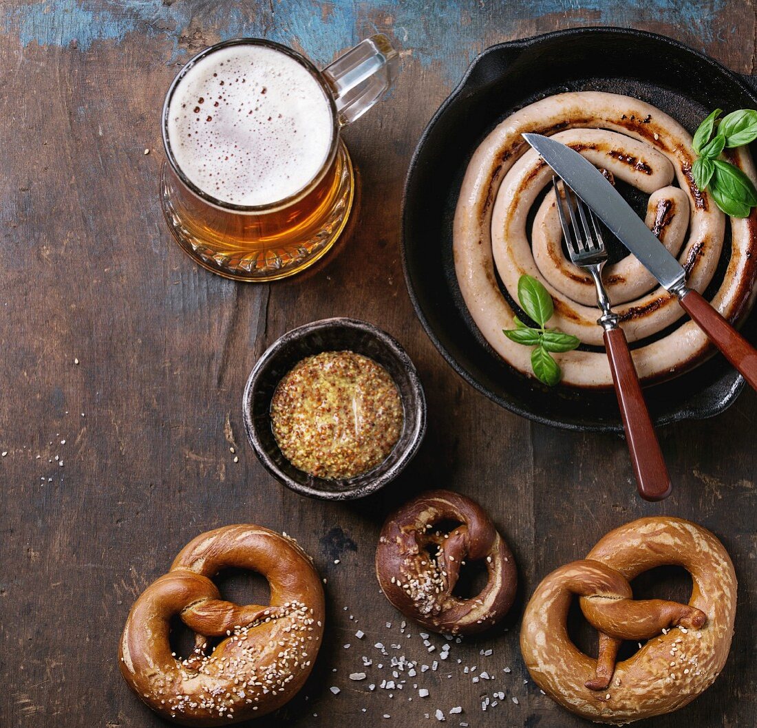 Bratwurstschnecke in der Pfanne dazu Bier, Senf und Brezen