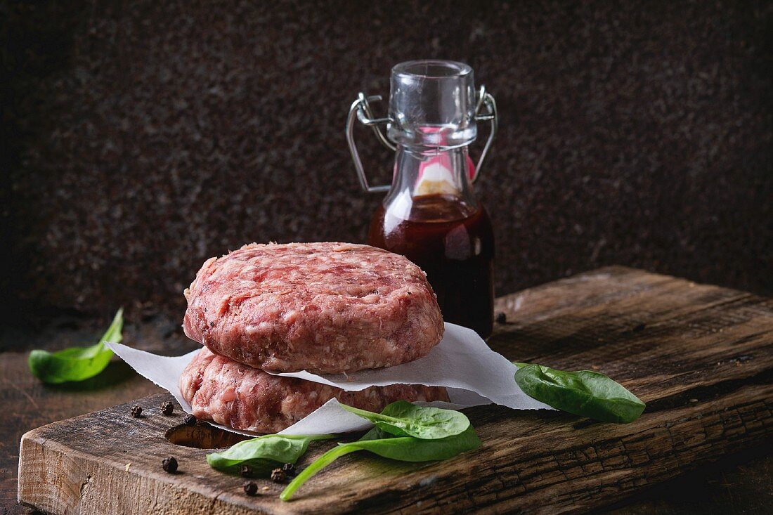 Zutaten für Hamburger: Rohe Patties, Spinat und Ketchupsauce auf Holzschneidebrett