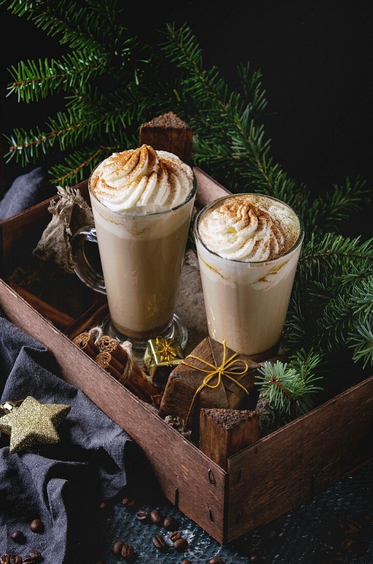 Pumpkin spicy latte with whipped cream and cinnamon in two glasses standing in wooden board with Christmas decoration