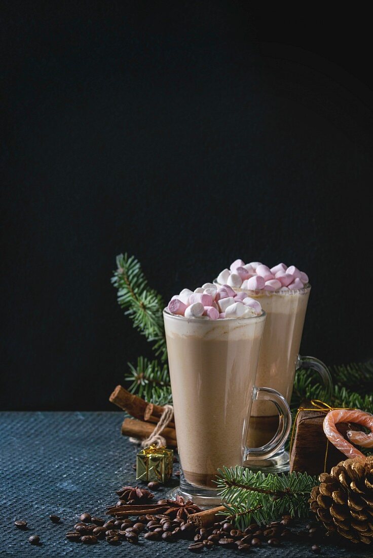 Two glasses of cafe latte with pink marshmallow with Christmas decor, candies, spices, coffee beans and fir tree