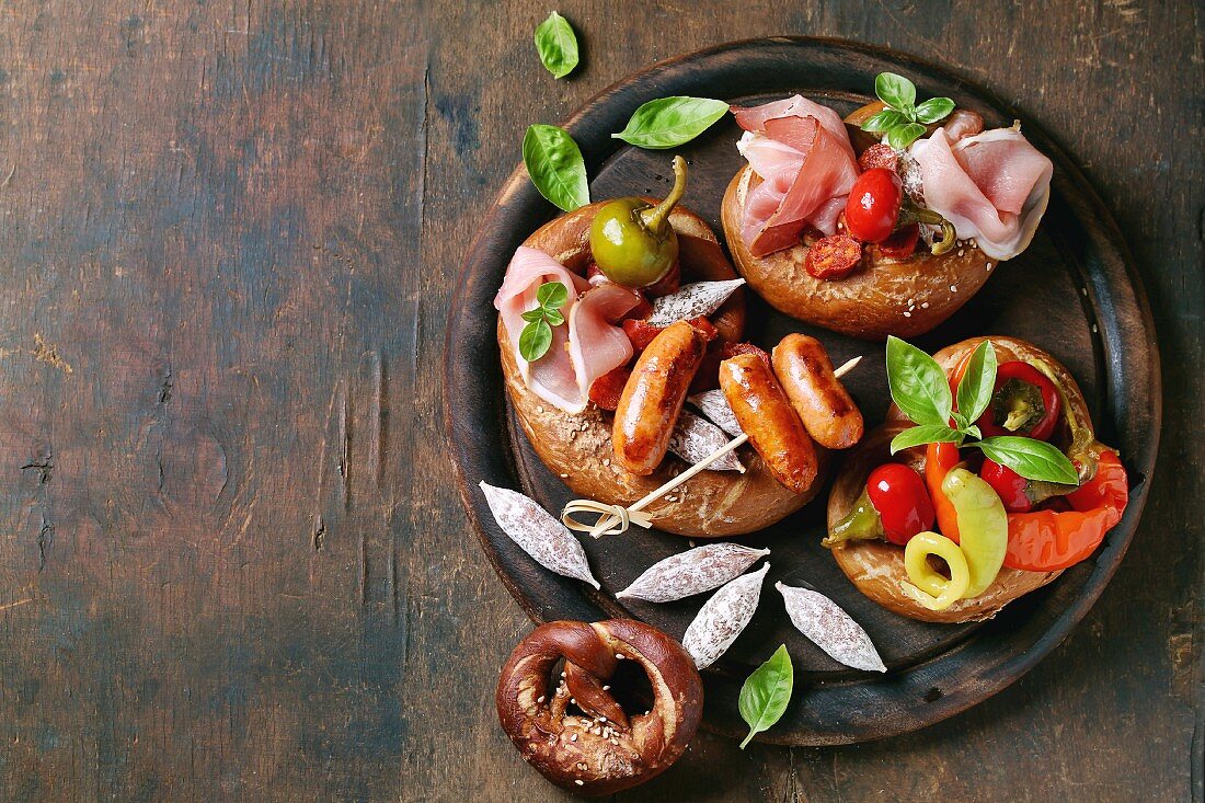 Fried sausages, wienerwurst, ham, marinated chili peppers served in salted pretzels with fresh basil