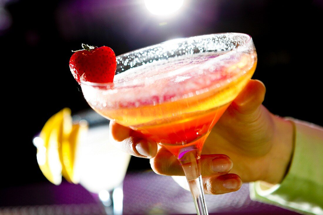 Womans hand holding a strawberry bellini cocktail in a bar