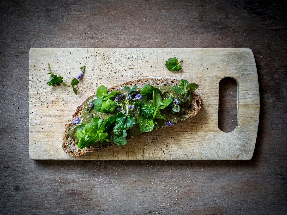 Scheibe Brot mit Wildkräutern auf einem Holzbrett (Aufsicht)