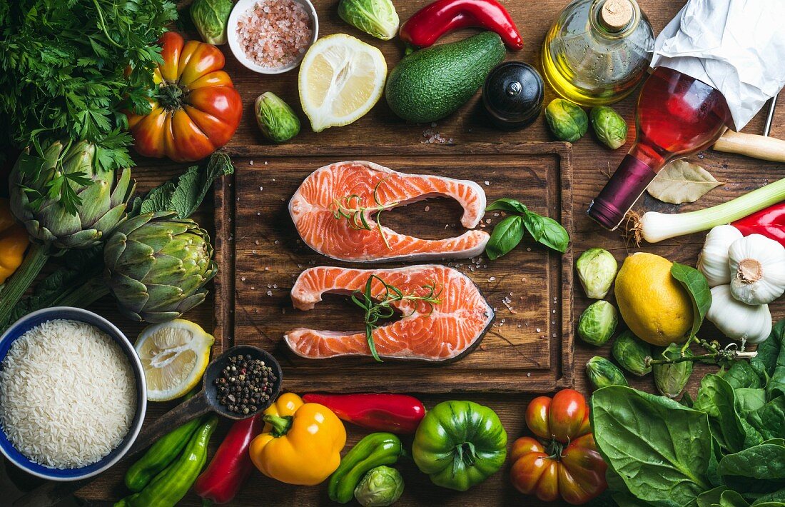 Raw uncooked salmon steak with vegetables, rice, herbs, spices and wine bottle on chopping board