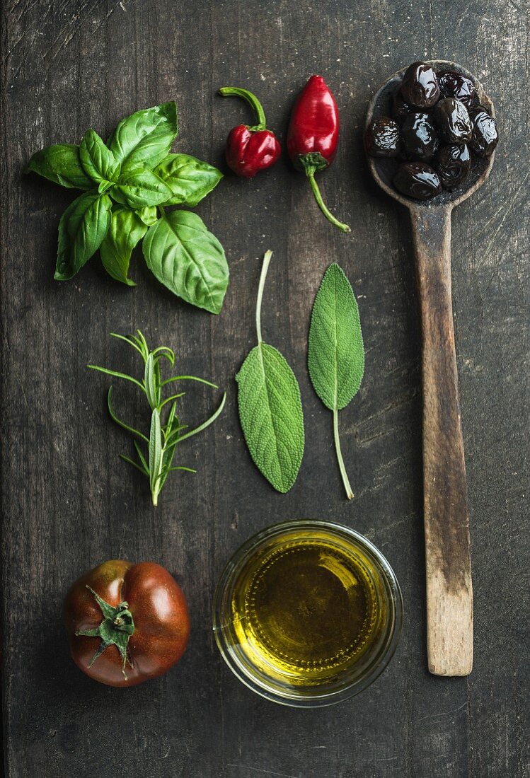 Greek black olives, fresh green sage, rosemary, basil herbs, oil, tomato, peppers on wooden background
