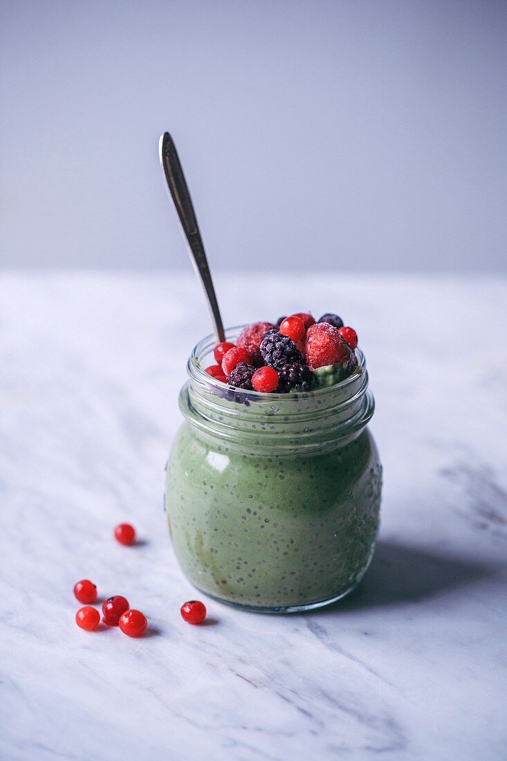 Matcha green tea chia pudding topped with frozen berries in a glass jar