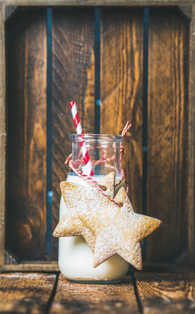 Bottle with milk and Christmas festive gingerbread star shaped cookies with decoration rope on wooden background