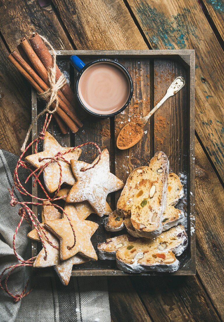 Tasse Kakao, Lebkuchen in Sternenform, Stollen und Zimtstangen auf Holztablett