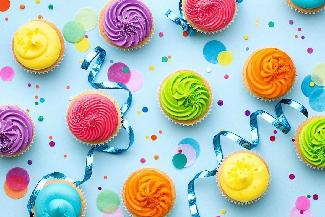 Verschiedene bunte Party-Cupcakes mit Partydeko auf blauem Untergrund