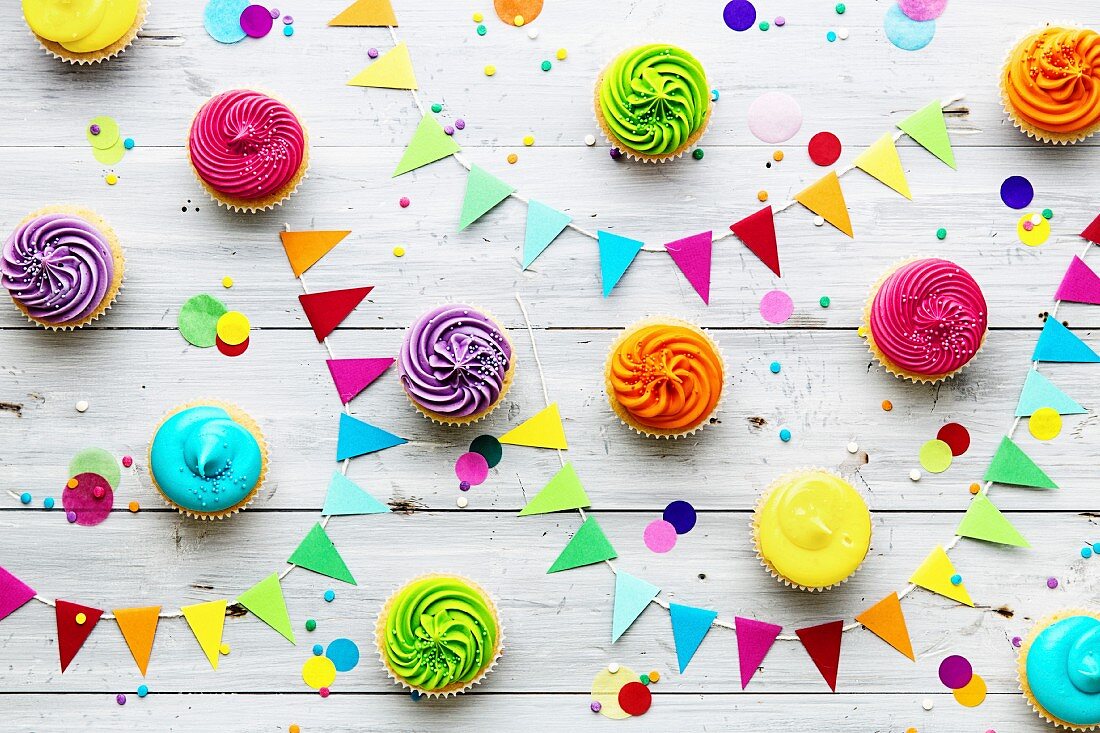 Verschiedene bunte Party-Cupcakes mit Partydeko auf Holzuntergrund