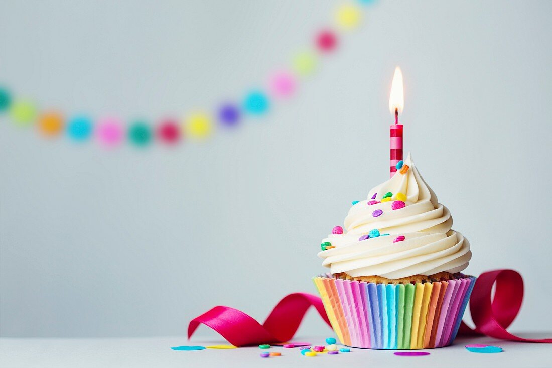 Geburtstags-Cupcake mit brennender Kerze und bunten Zuckerstreuseln