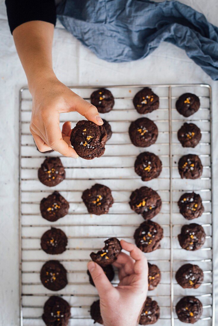 A woman s hand and a man s hand grabbing chocolate citrus cookies from a wire rack