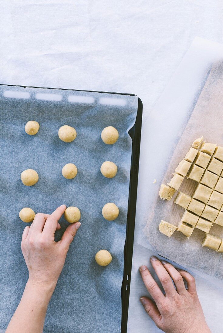 Hands placing cookie balls in a baking pan