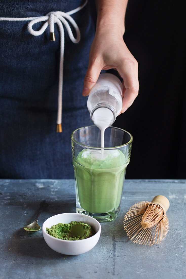 Female hands pouring coconut milk into matcha latte