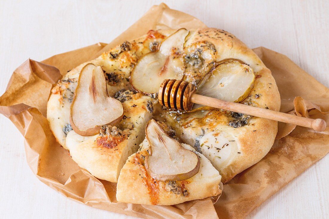 Sliced Pizza with pear, gorgonzola and honey with olive wood honey dipper on baking paper