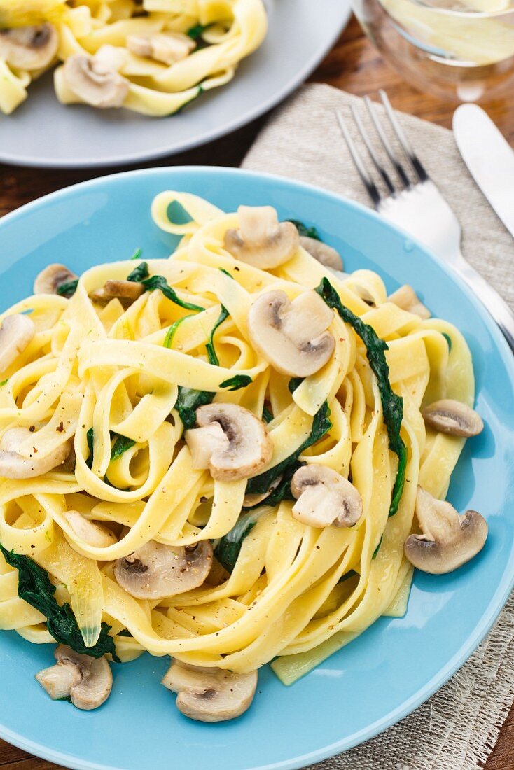 Fettuccine with spinach and mushrooms on a blue plate