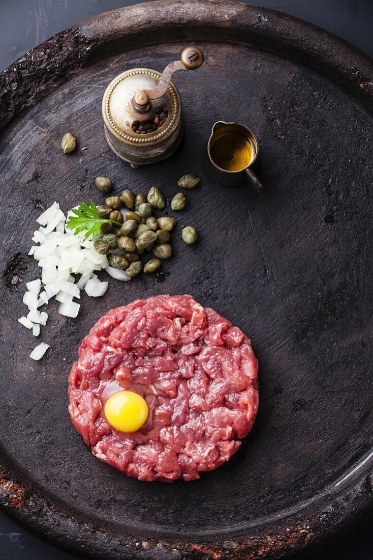 Beef tartar with capers and fresh onions on black textured background