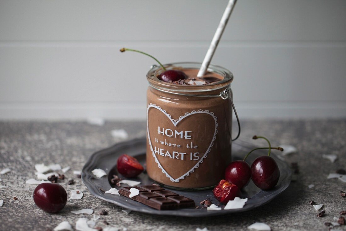 Chocolate coconut smoothie in a jar topped with cherry, dark chocolate, coconut flakes and cacao nibs