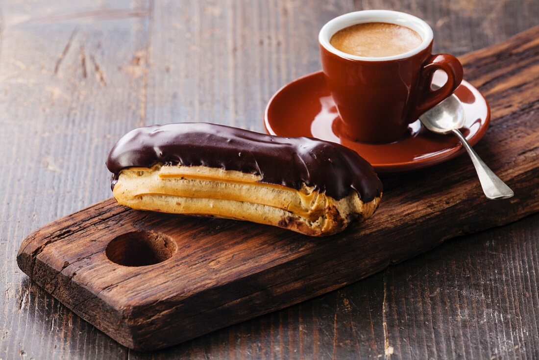 Schokoladen-Eclair und Tasse Kaffe auf Holzbrett