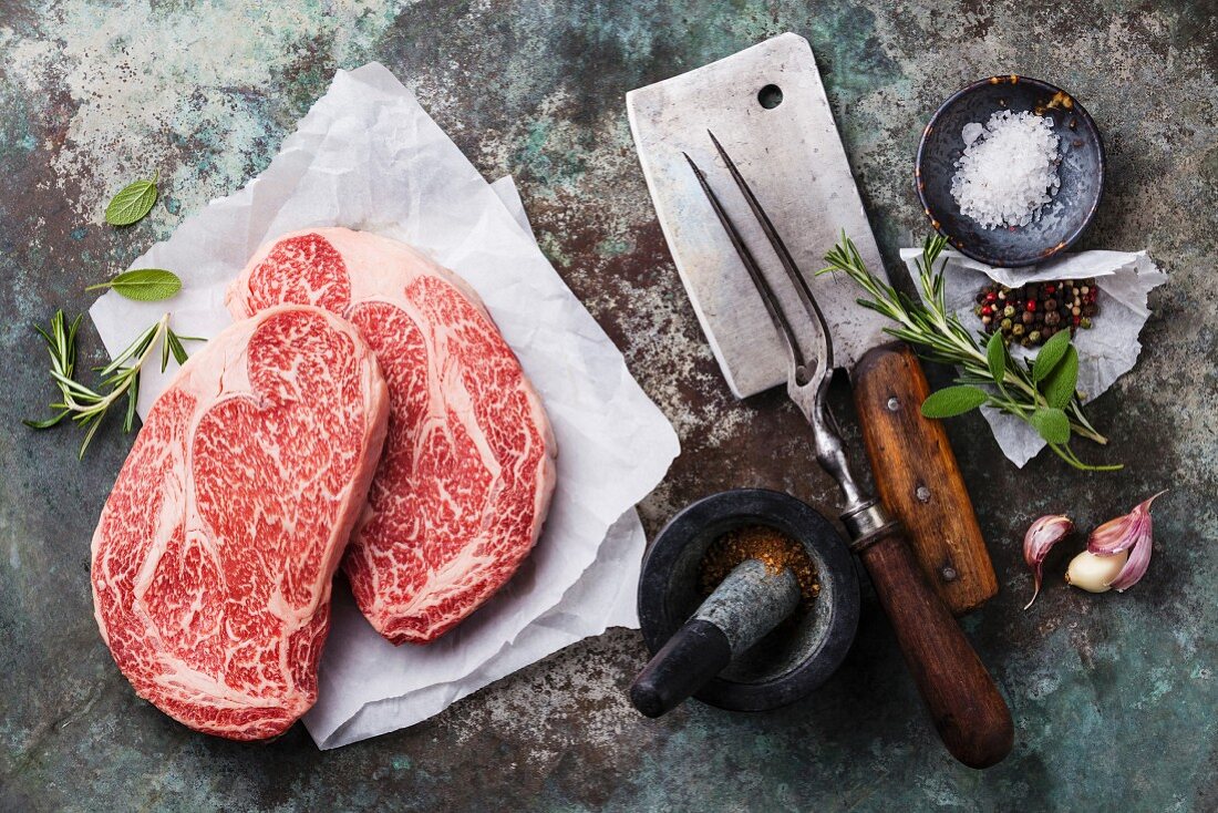 Rohe marmorierte Black Angus Steaks mit Gewürzen und Küchenutensilien