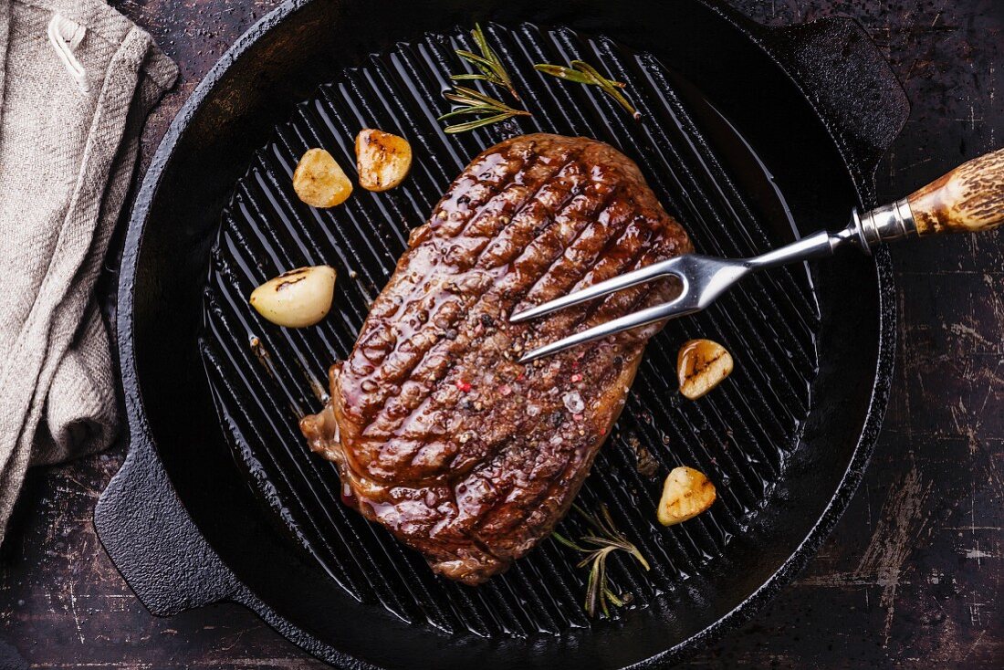Grilled Ribeye steak and meat fork on grill pan on dark background