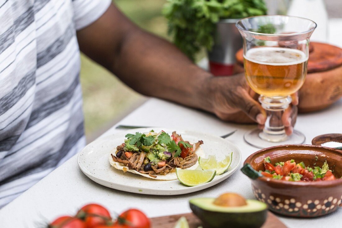 Dunkelhäutiger Mann mit Rindfleisch-Taco und Bier an Tisch im Freien