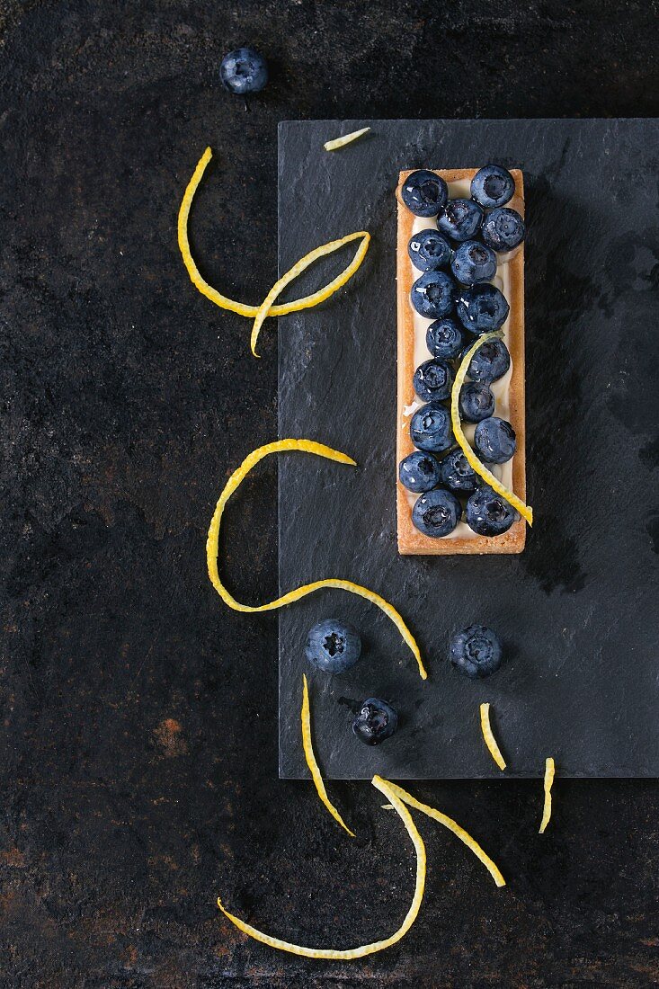 Zitronentörtchen mit Blaubeeren auf schwarzem Untergrund