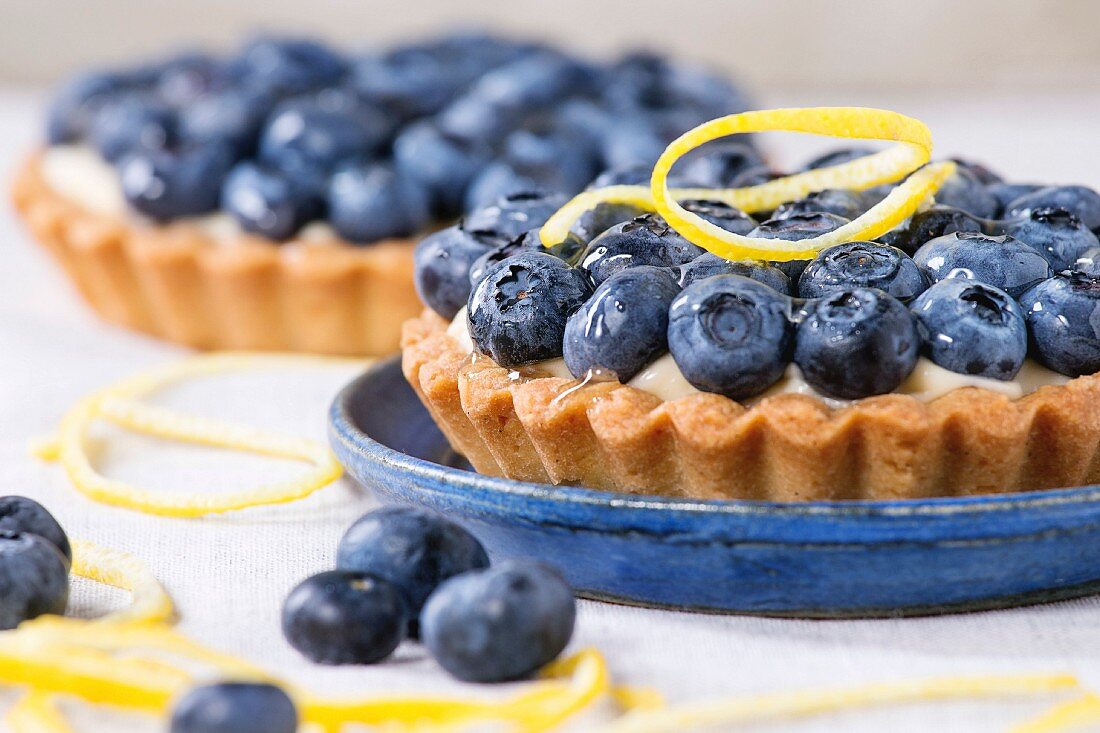 Close up of Two Lemon tartlets with fresh blueberries, served on blue ceramic plate