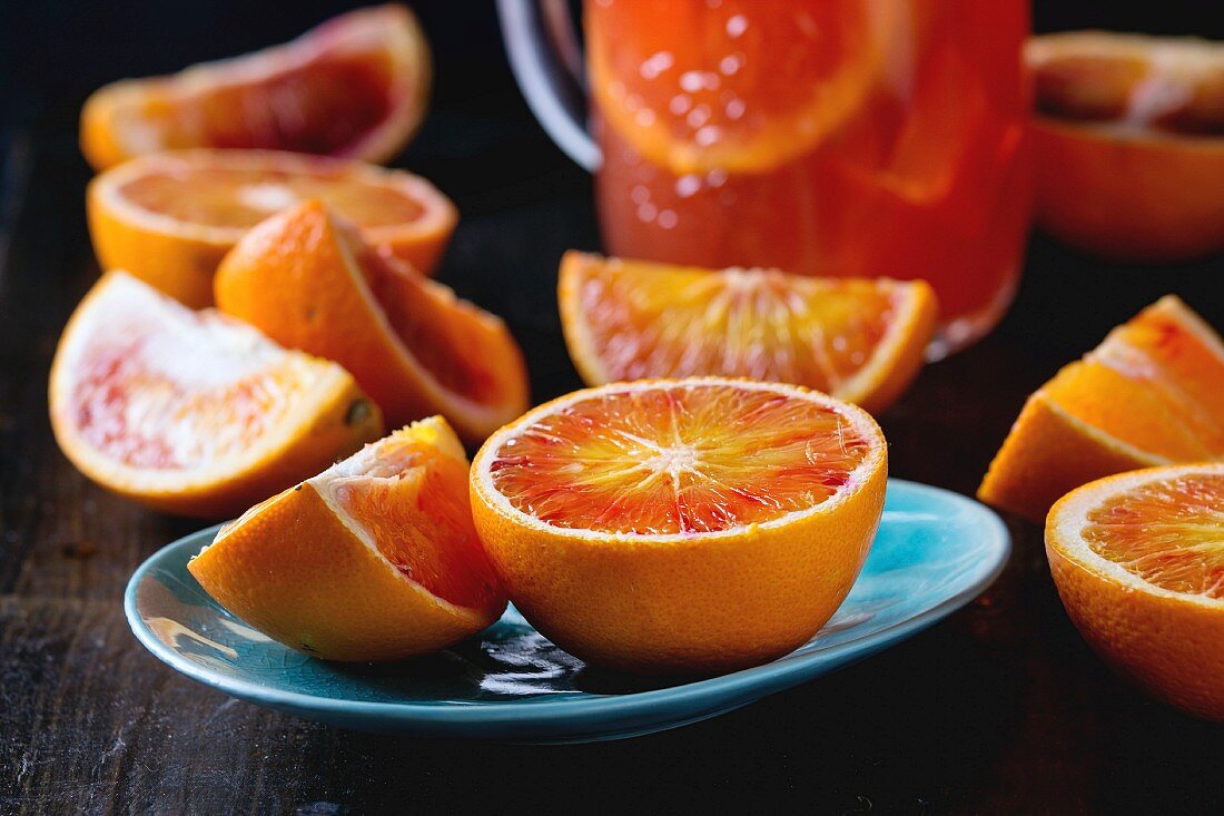 Sliced Sicilian Blood oranges in turquoise ceramic plate and glass mason jar of fresh red orange juice