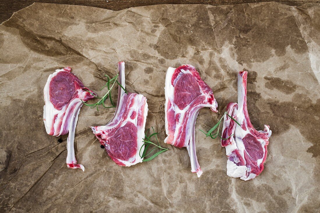Raw lamb chops. Rack of Lamb with rosemary and spices over oily craft paper background