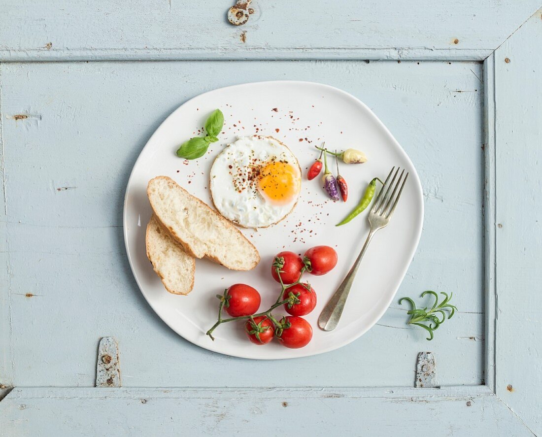 Breakfast set. Fried egg, bread slices, cherry tomatoes, hot peppers and herbs on white ceramic plate