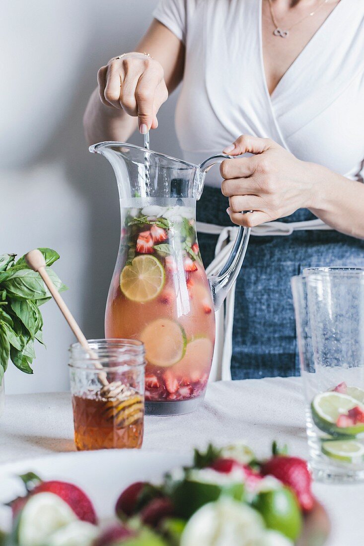 Frau mischt Honig gesüsste Limeade mit Erdbeeren und Basilikum im Glaskrug