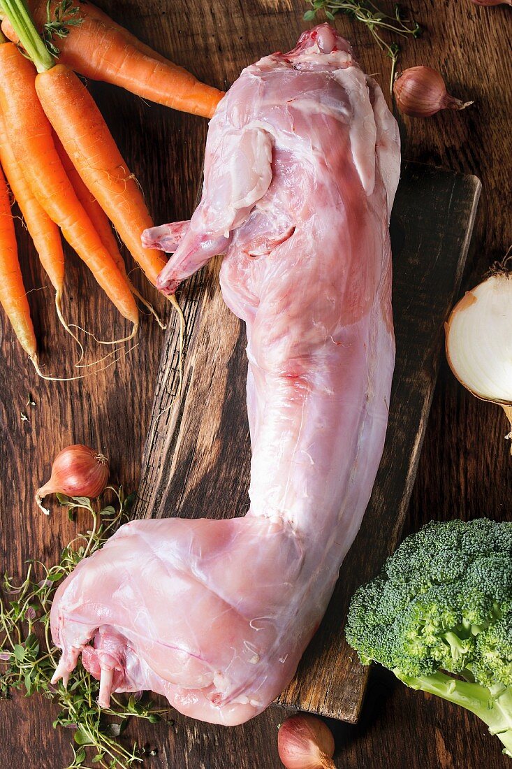 Raw uncooked whole rabbit with fresh vegetables and herbs on wooden chopping board