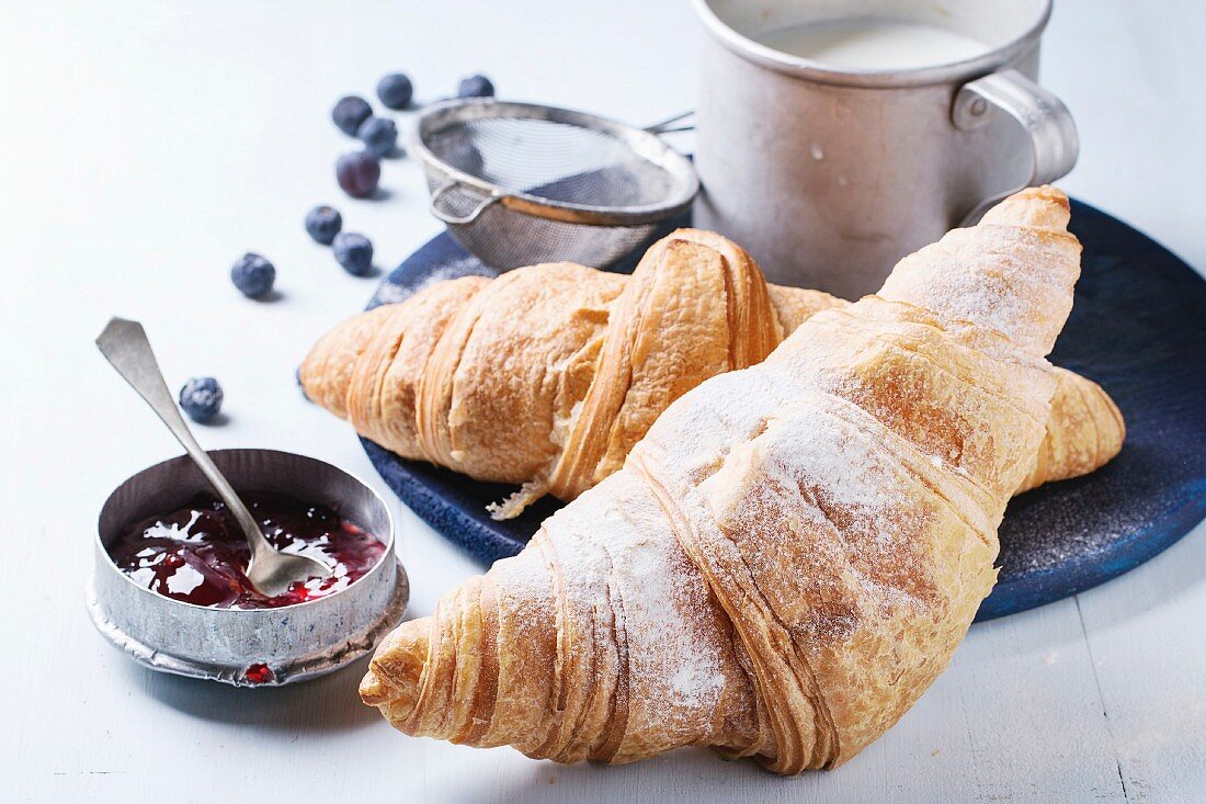 Two fresh baked croissants with sugar powder served with jam, aluminum cup of milk