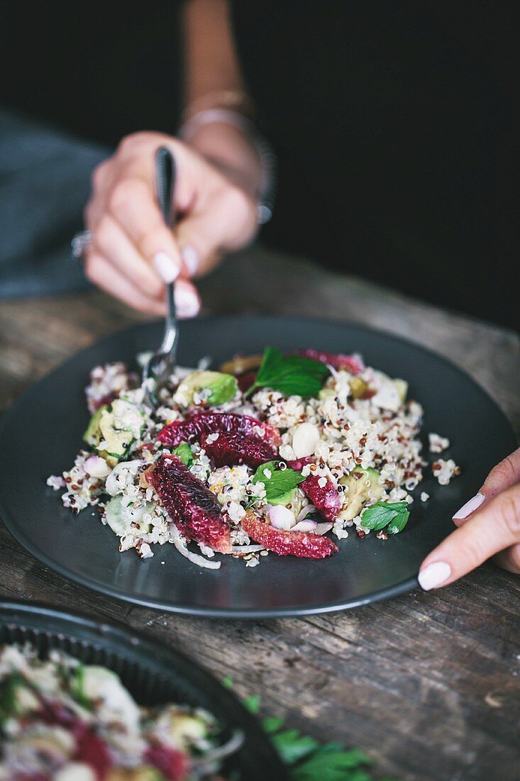 A woman is eating avocado and quinoa salad with blood oranges and fennel