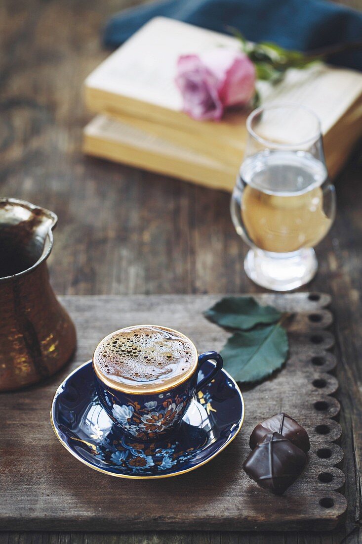 A cup of Turkish coffee with foam on top is photographed on a vintage wood plate
