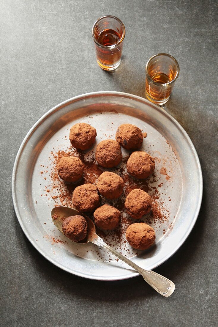 Chocolate truffles on an aluminum plate with two glasses of liqueur on background