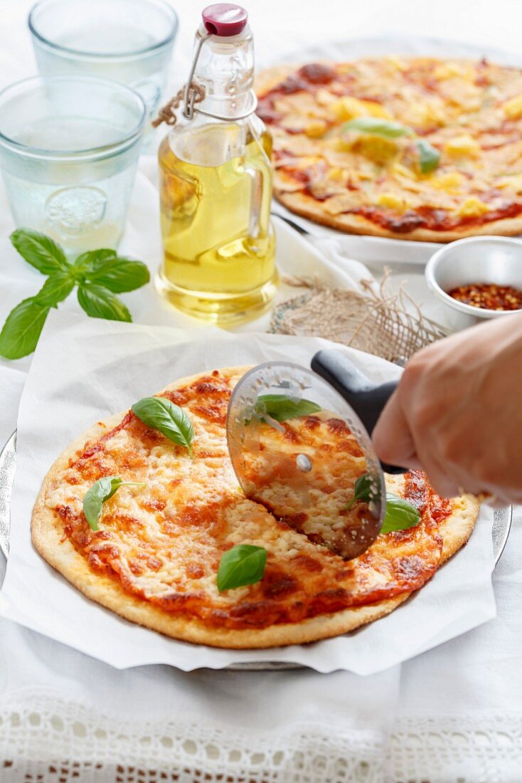 Pizza Margherita wird mit Pizzaschneider geschnitten