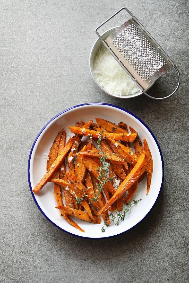 Sweet potato fries in an enamel plate with grated parmesan, spices and thyme