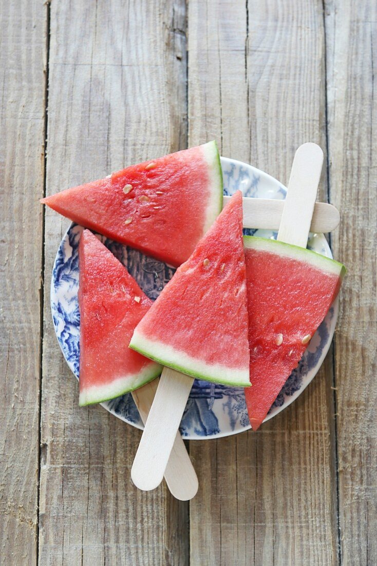 Wassermelonestücke mit Holzstielen auf Teller