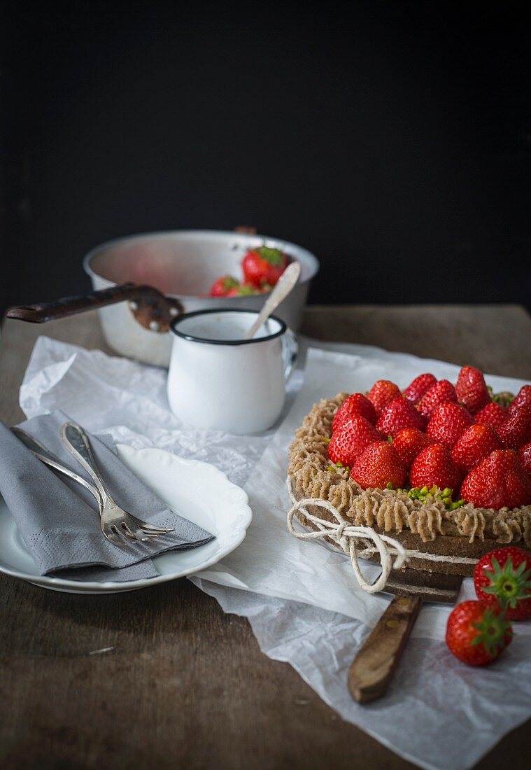 Strawberry tart with ribbon on wooden table with dishes