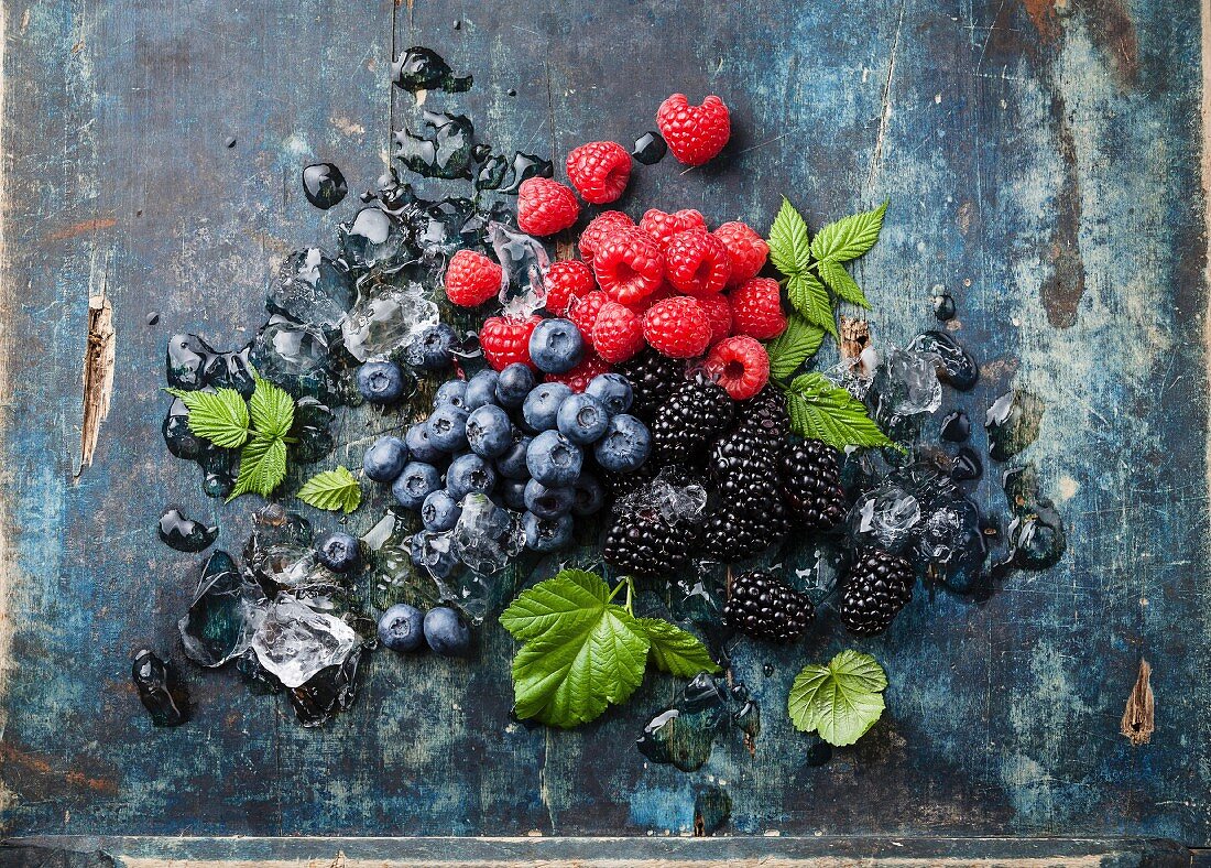 Mix of fresh berries with ice on blue wooden background