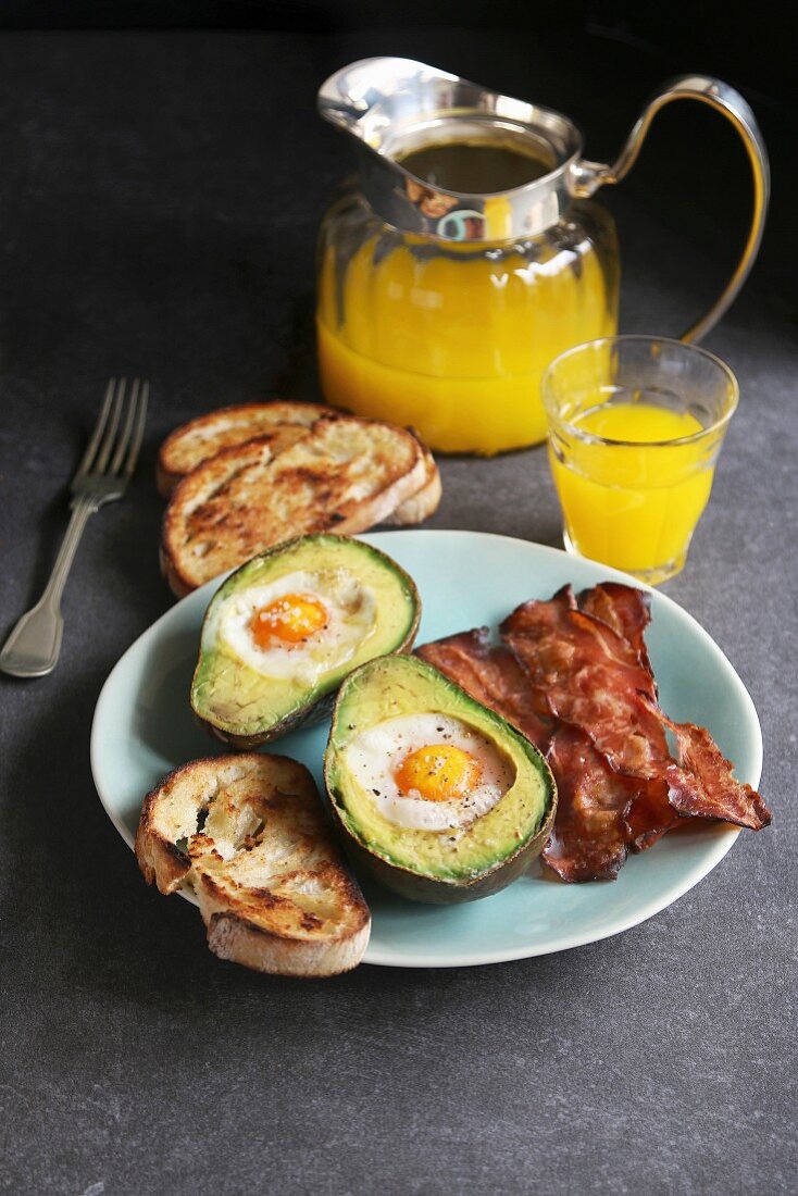 Breakfast with eggs baked in avocado, bacon, bread toast and orange juice